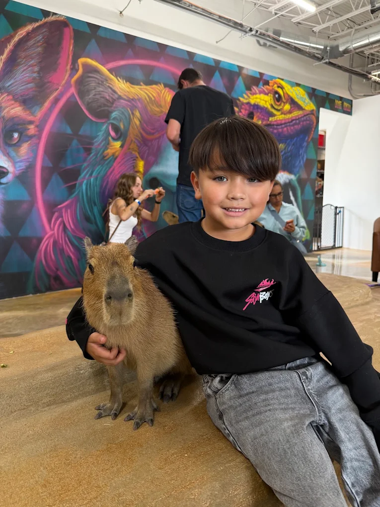 A young guest sitting with a capybara in front of our animal mural