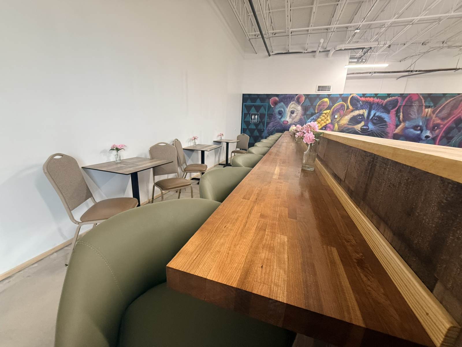 Bar rail seating with green stools facing the animal mural